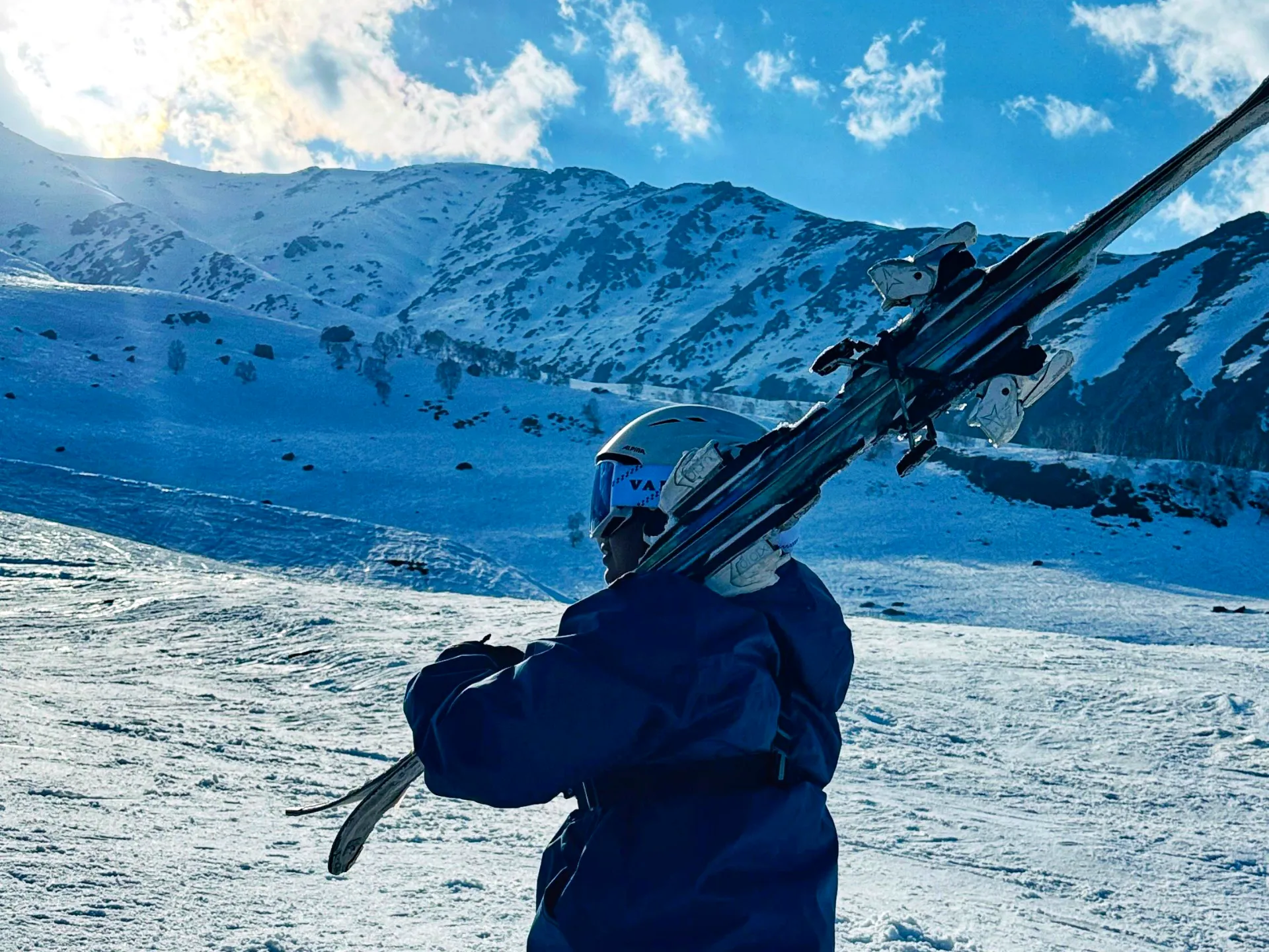 A skier carrying skis across a Gulmarg slope